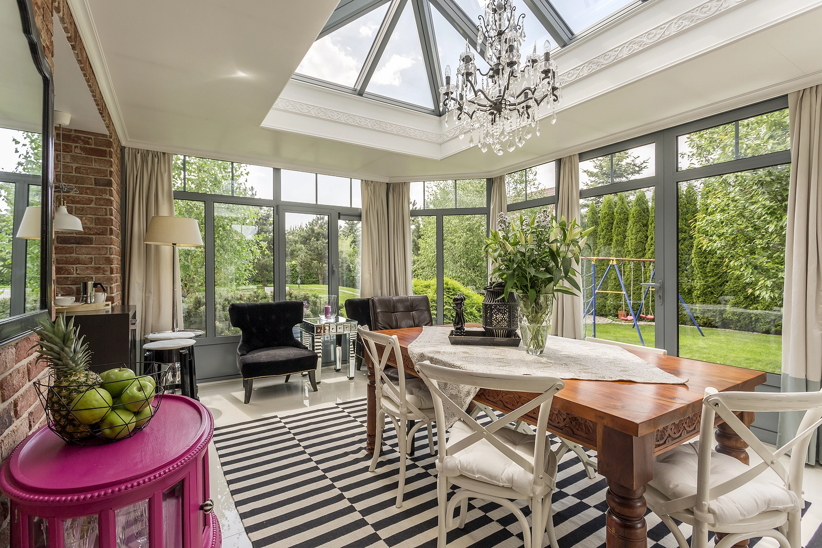 Sunroom remodel with glass ceiling, chandelier, wood table, and backyard view